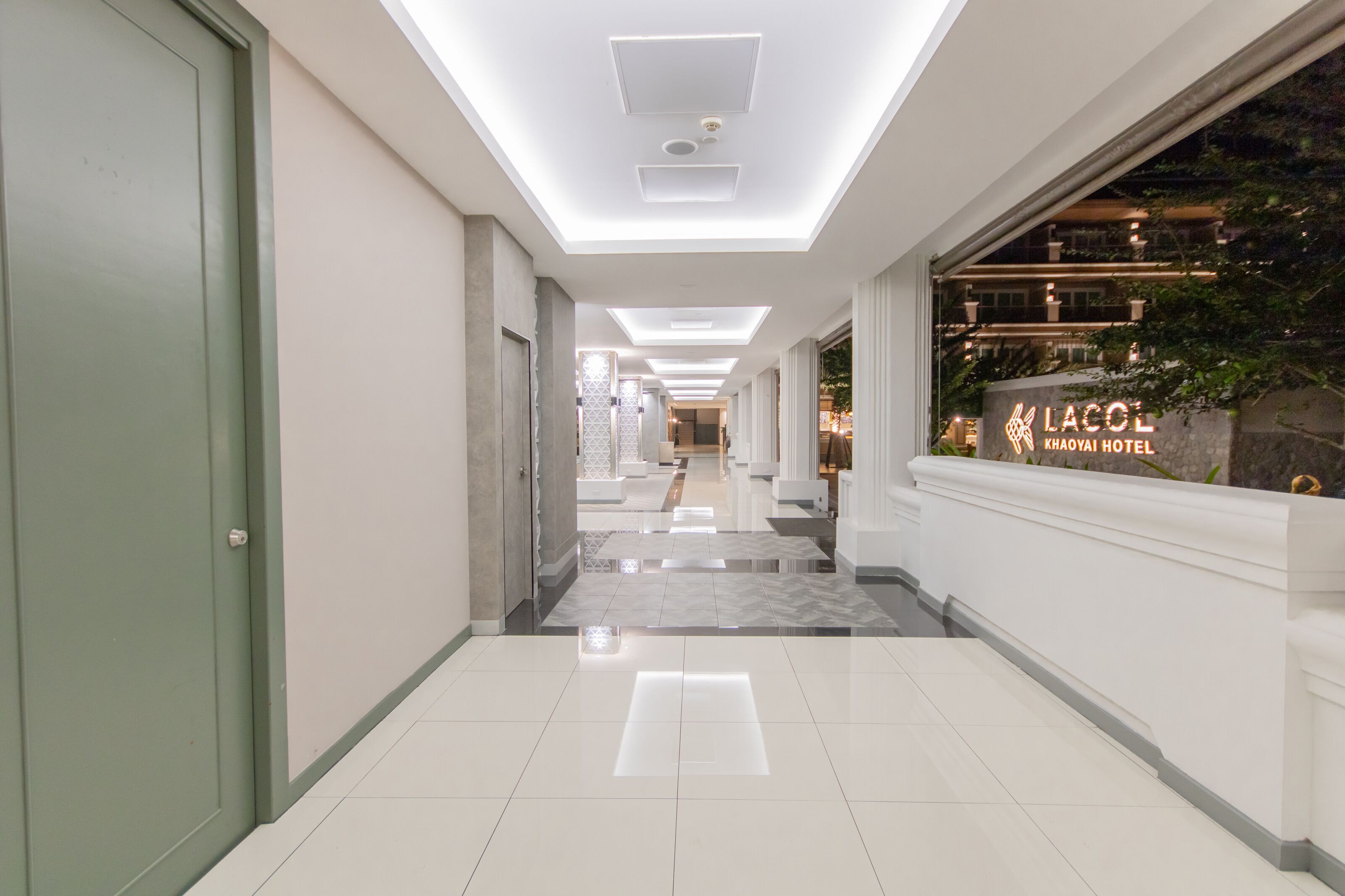A hotel corridor with a modern design, featuring a clean, tiled floor and recessed lighting on the ceiling.