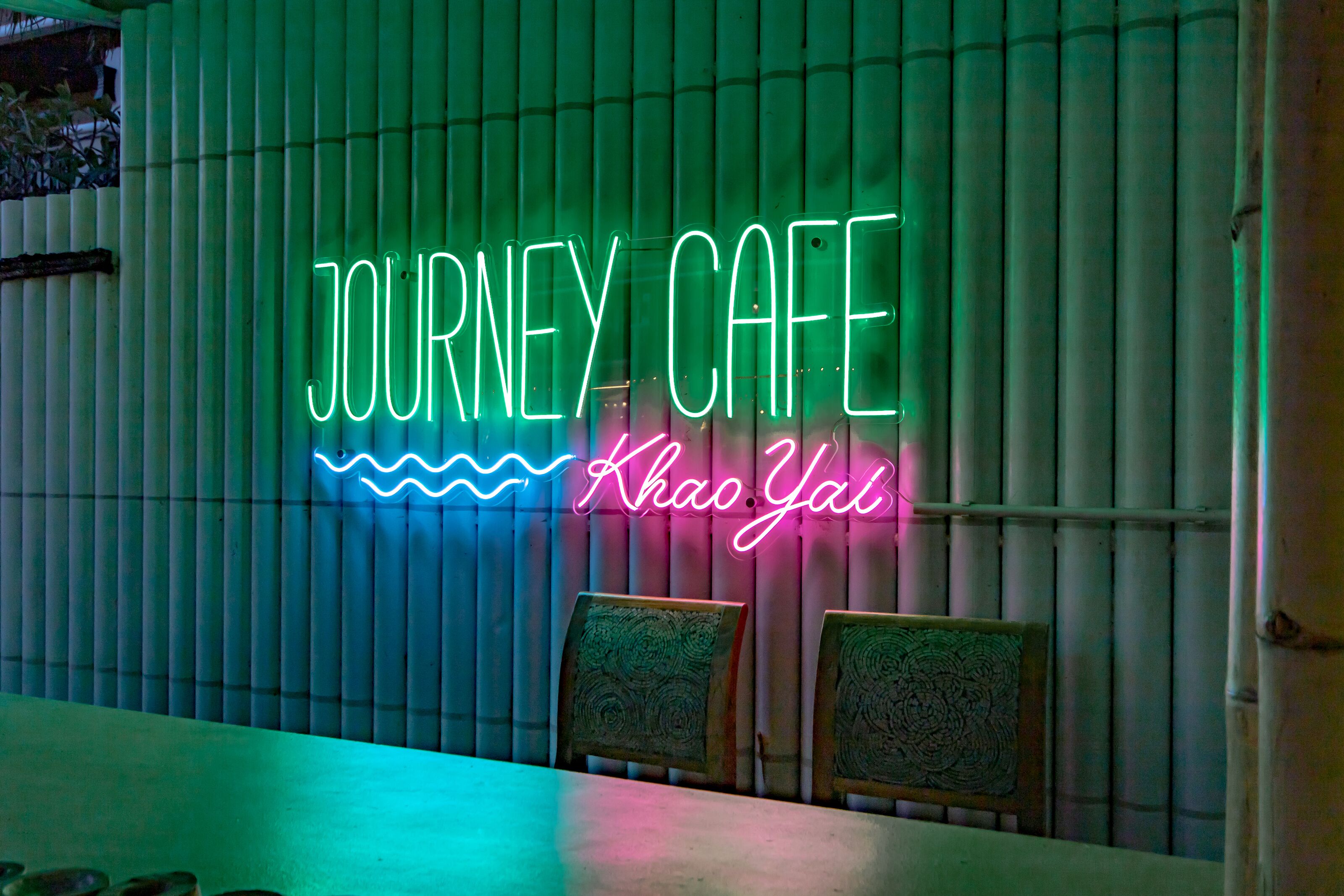Neonbord met de tekst 'JOURNEY CAFE', met een gestileerd golfpatroon, voor een wand van bamboe.