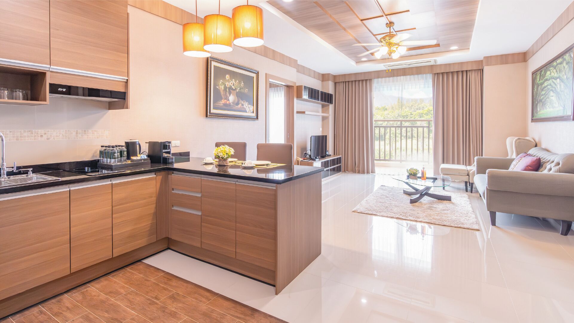 Een moderne keuken met houten kastjes, een eethoek met een glazen tafel, een bank en een balkon met gordijnen.