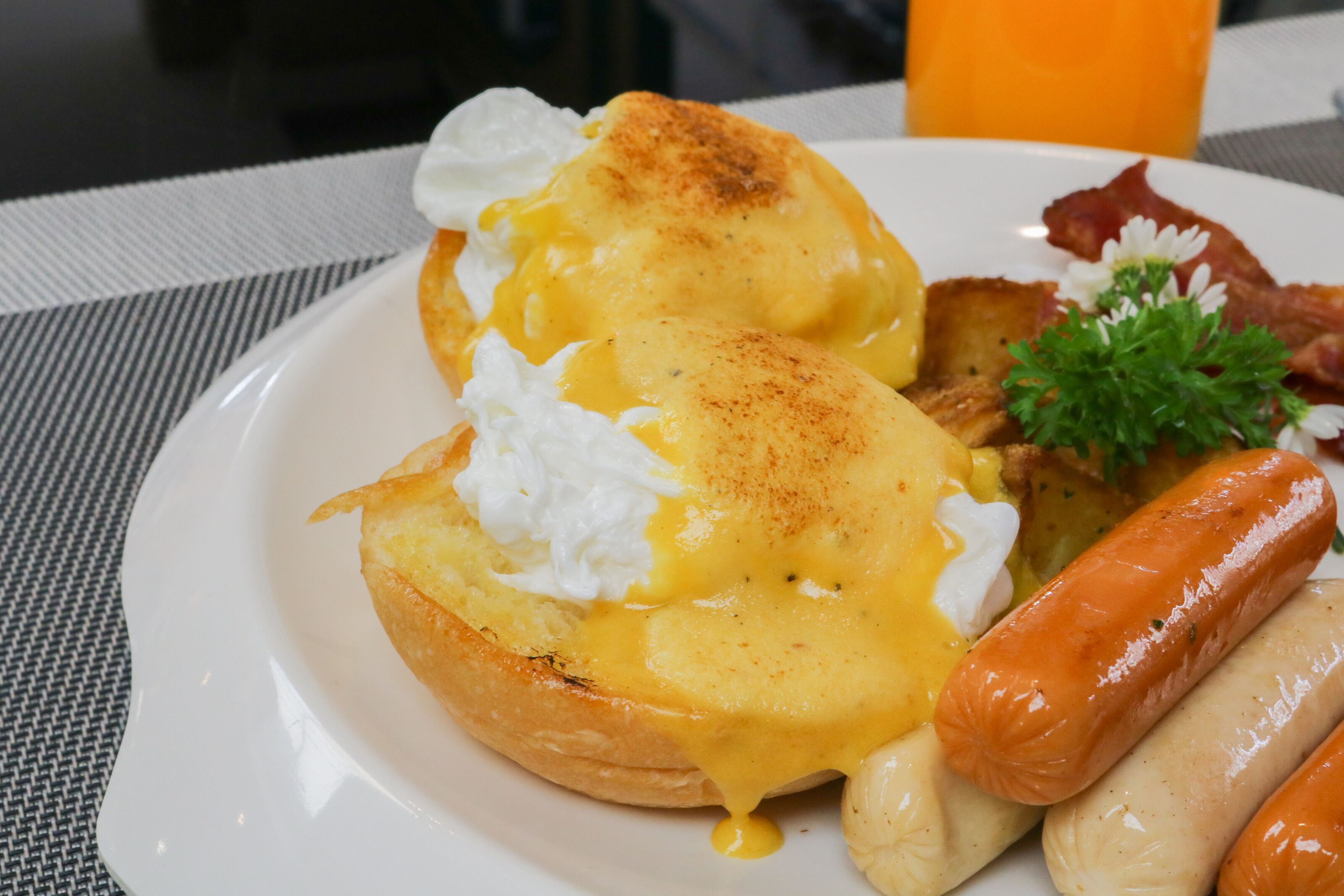 Un plato con huevos benedictinos, salchichas y tocino.