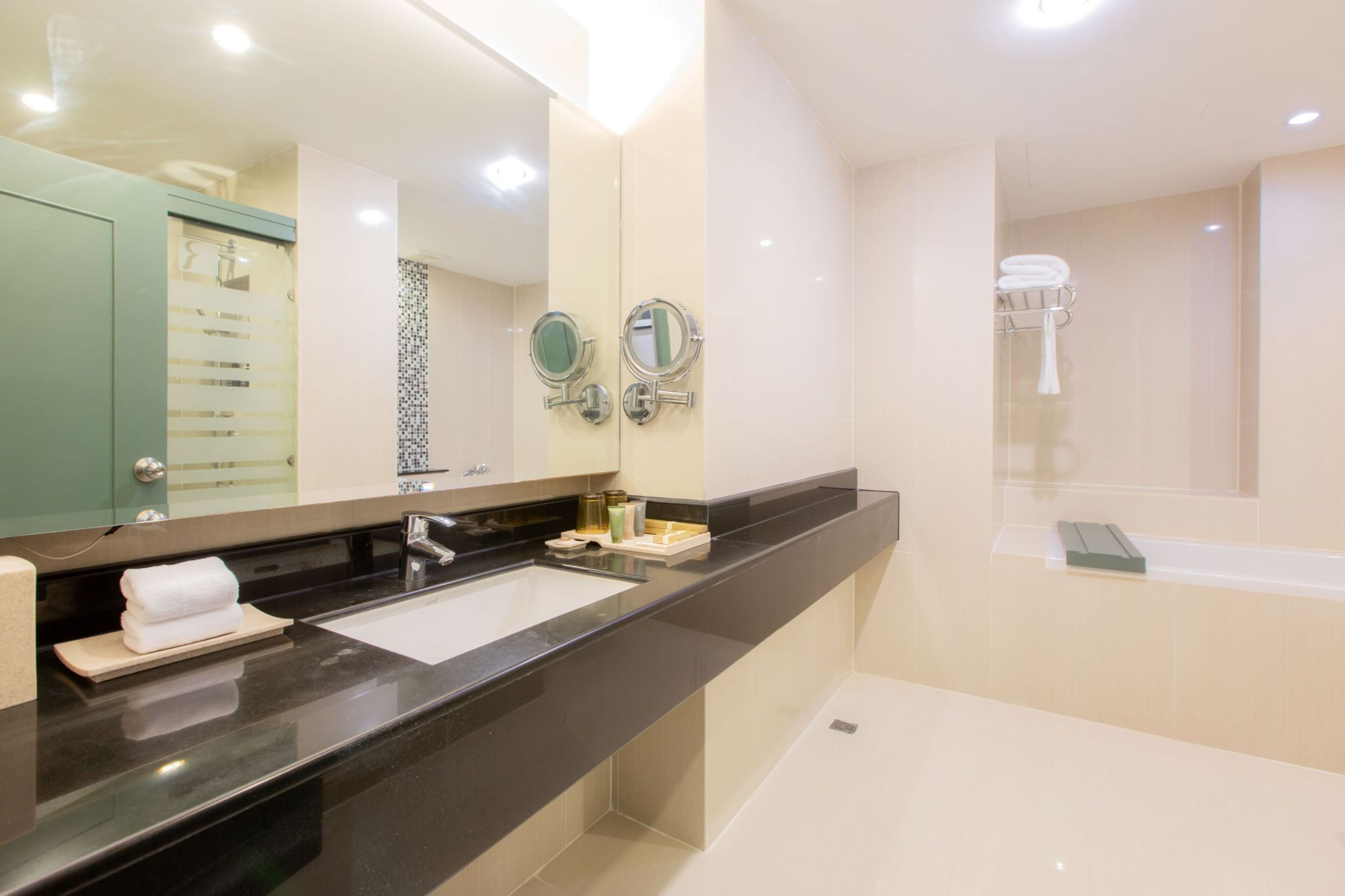 A modern bathroom with a black countertop, two sinks, a large mirror, and a bathtub.
