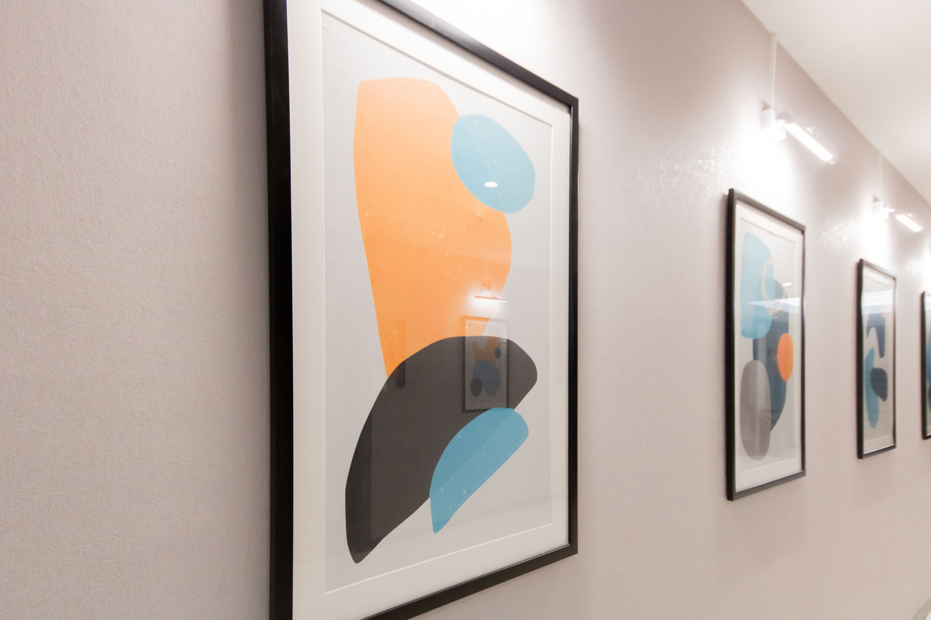 Ein Korridor mit gerahmten abstrakten Kunstwerken an der Wand.