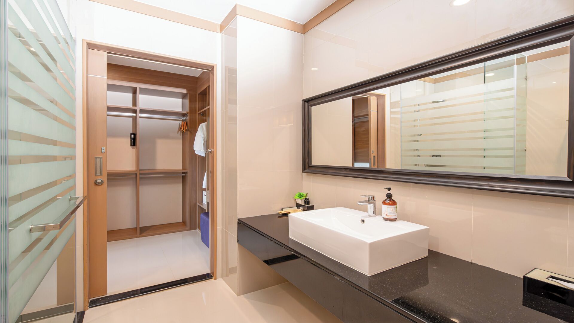Un baño moderno con un espejo grande, un lavamanos blanco y un vestidor.