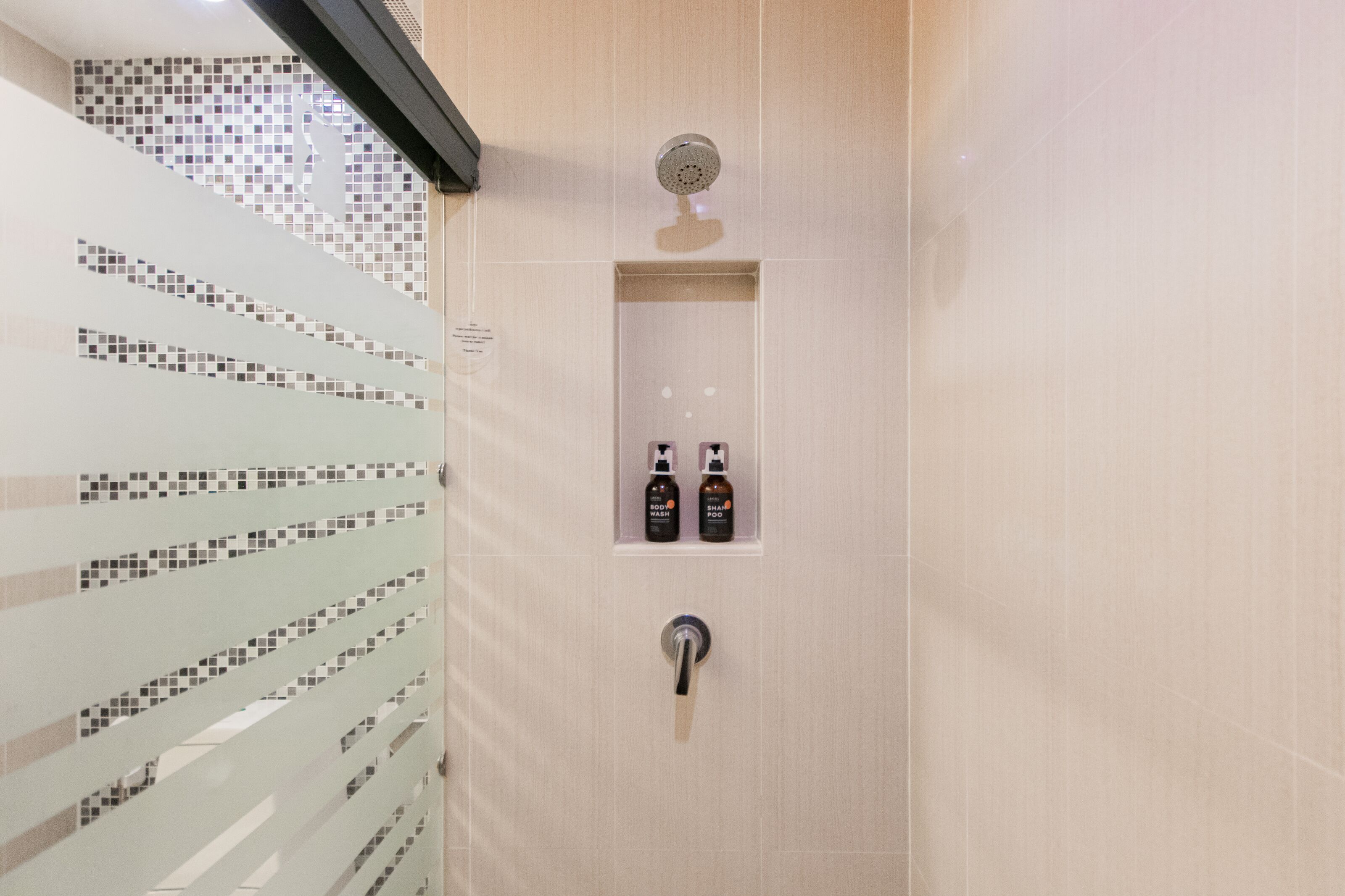 A shower with a tiled wall, a showerhead, and two bottles of shampoo and conditioner.