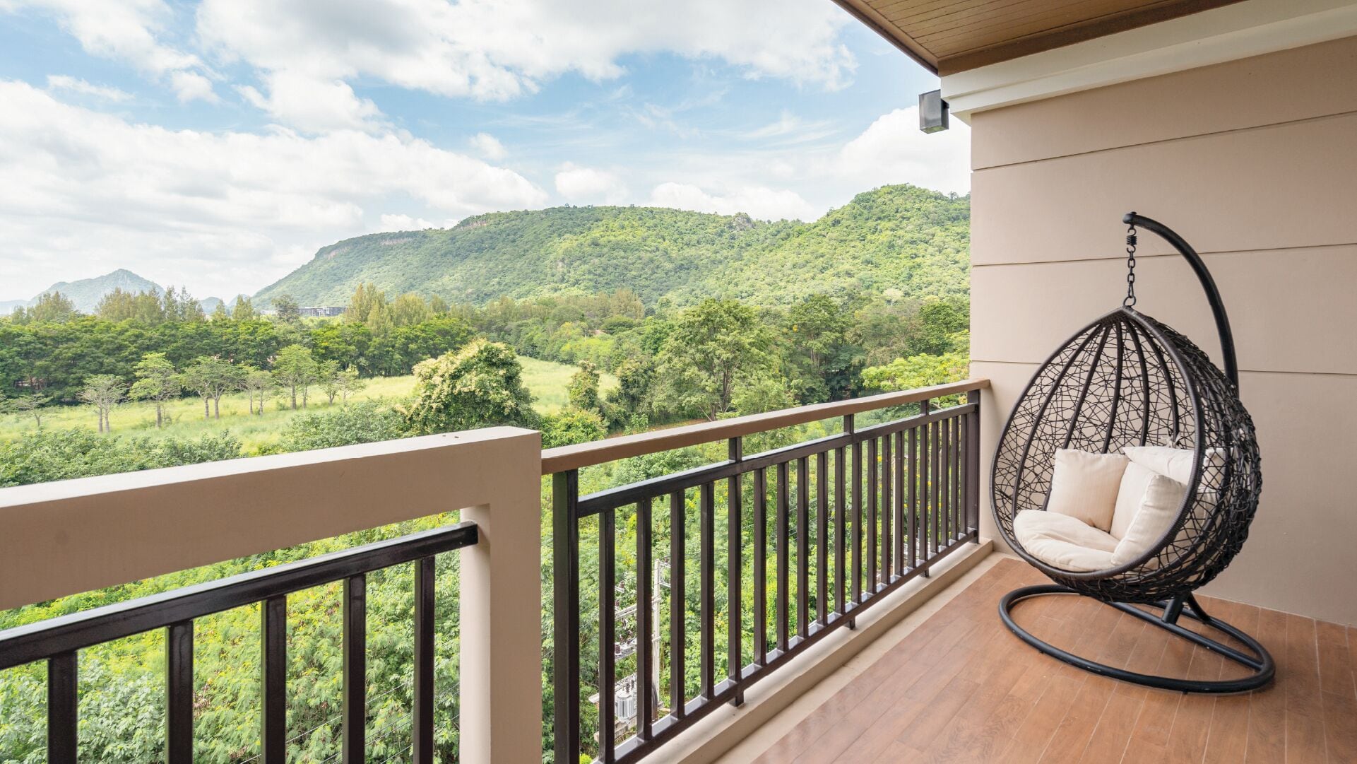 A balcony with a hanging chair, wooden floor, and a view of a green landscape.