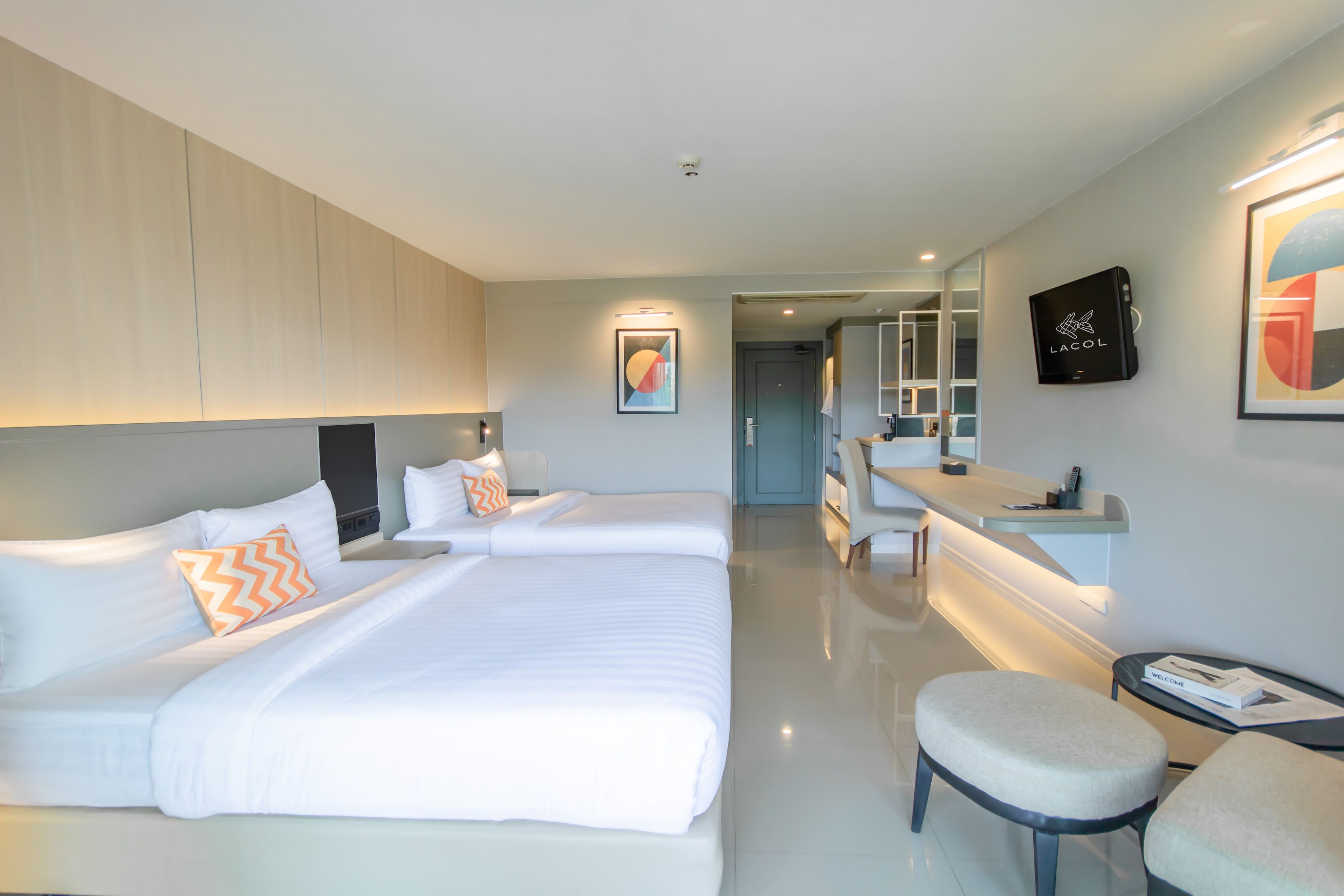A modern hotel room with two beds, a desk, a chair, and a small seating area.