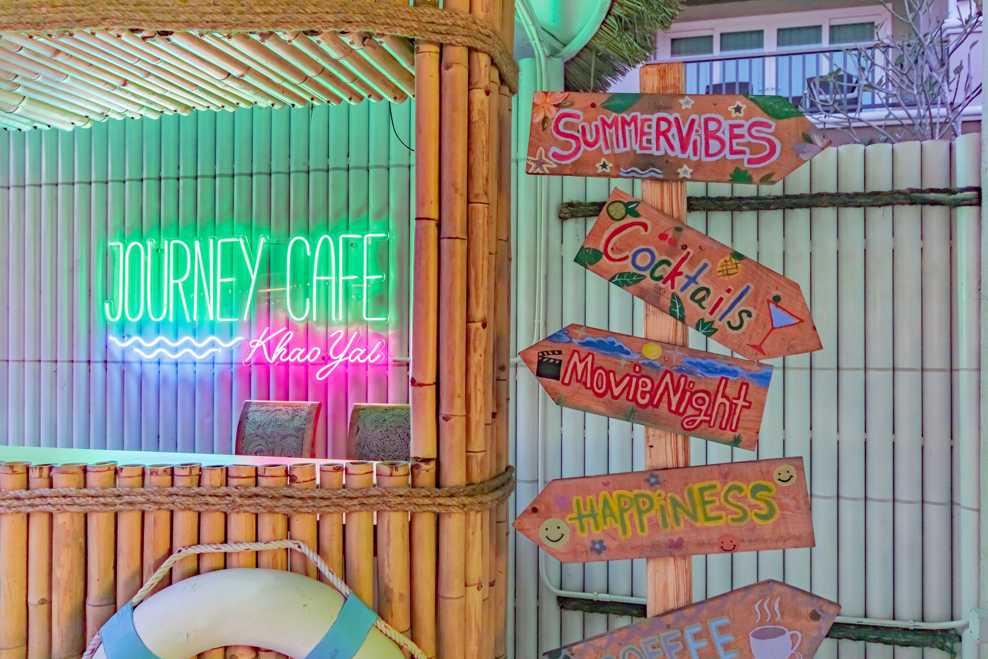 A neon sign reading "JOURNEY CAFE" with a wooden signpost featuring "SUMMERVIBES," "Cocktails," "Movie Night," "HAPPINESS," and "COFFEE."