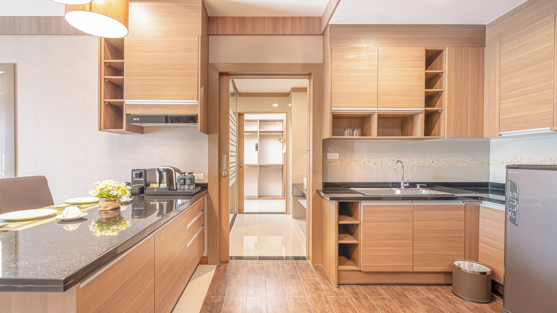 A modern kitchen with wooden cabinets, a stainless steel refrigerator, and a countertop with a coffee maker.