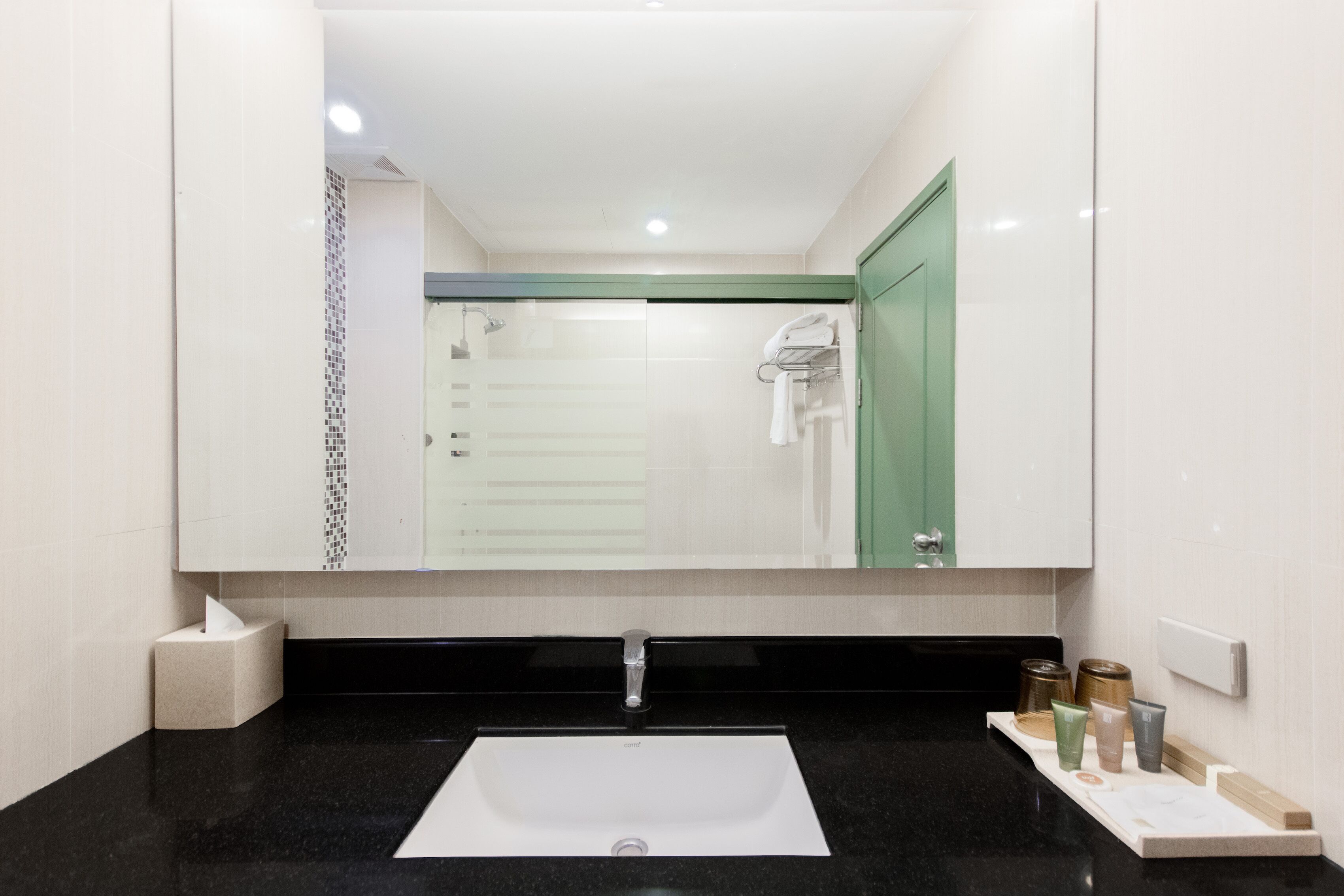A modern bathroom with a large mirror, a white sink, and a black countertop.