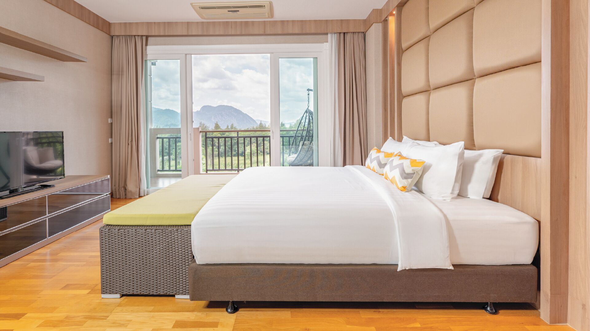 A hotel room with a large bed, a TV, and a balcony with a mountain view.