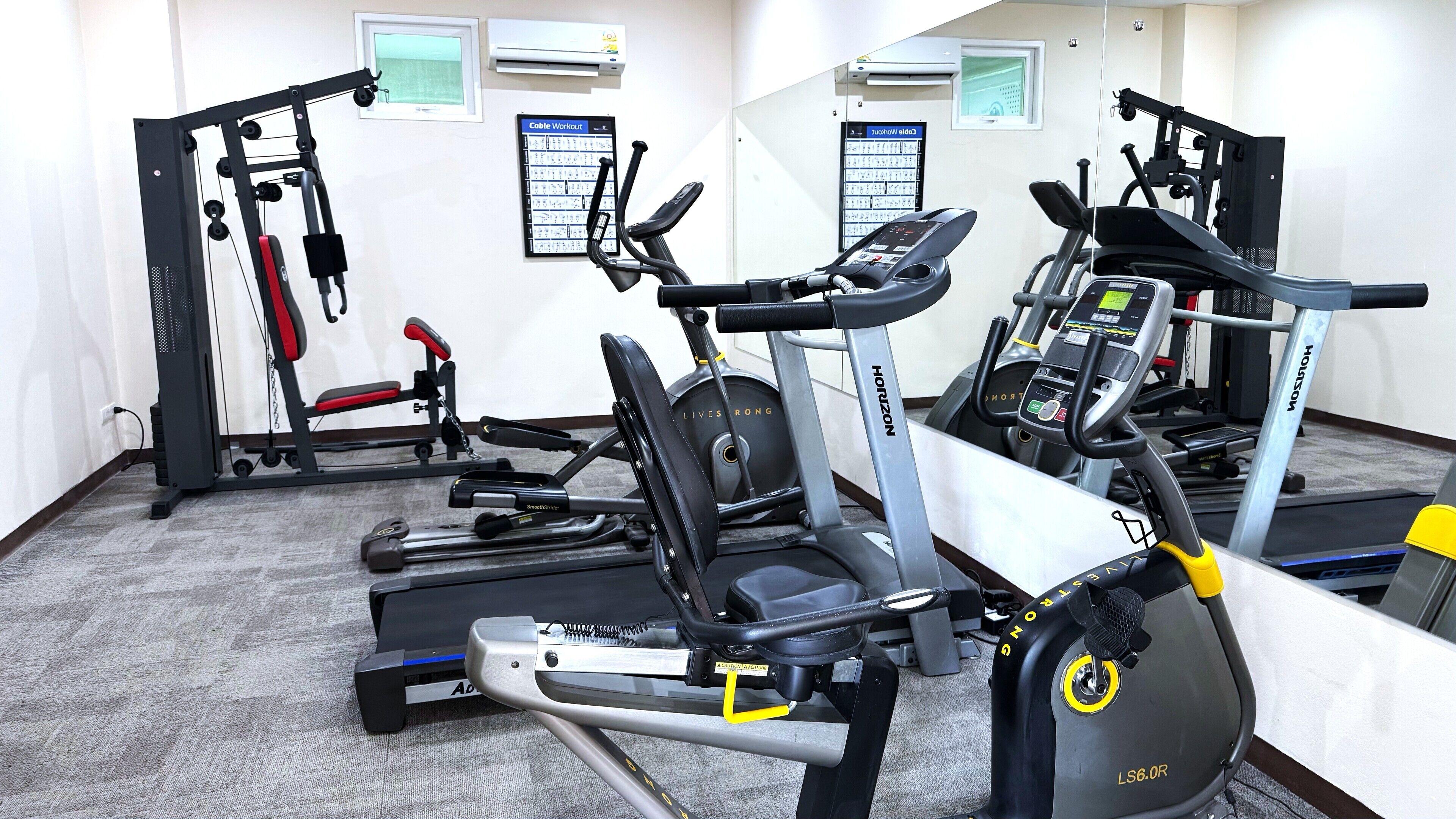 A gym with various exercise equipment including treadmills, a cable machine, and a weight bench.