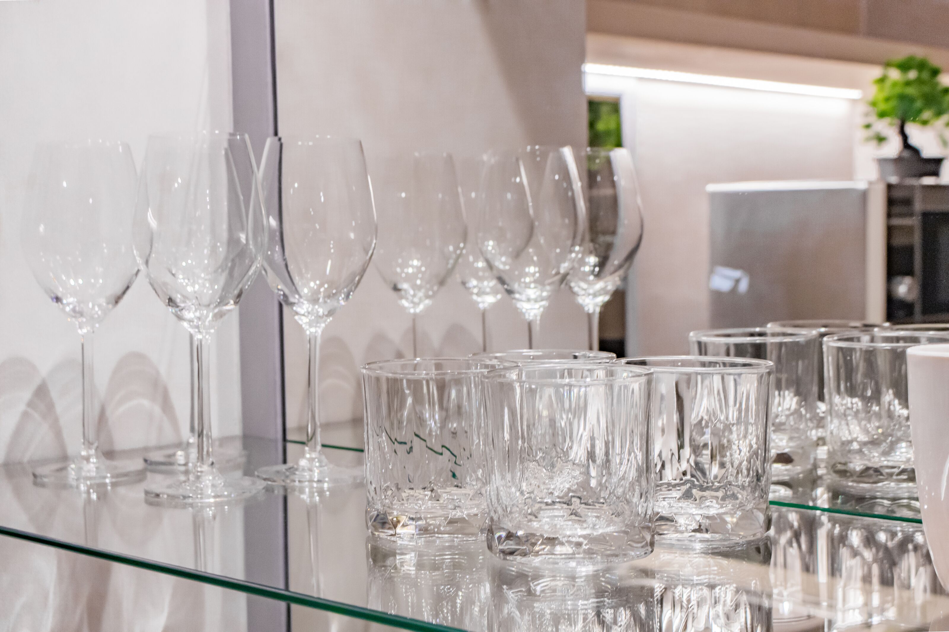 A row of empty wine glasses and tumblers on a glass table in a modern interior setting.