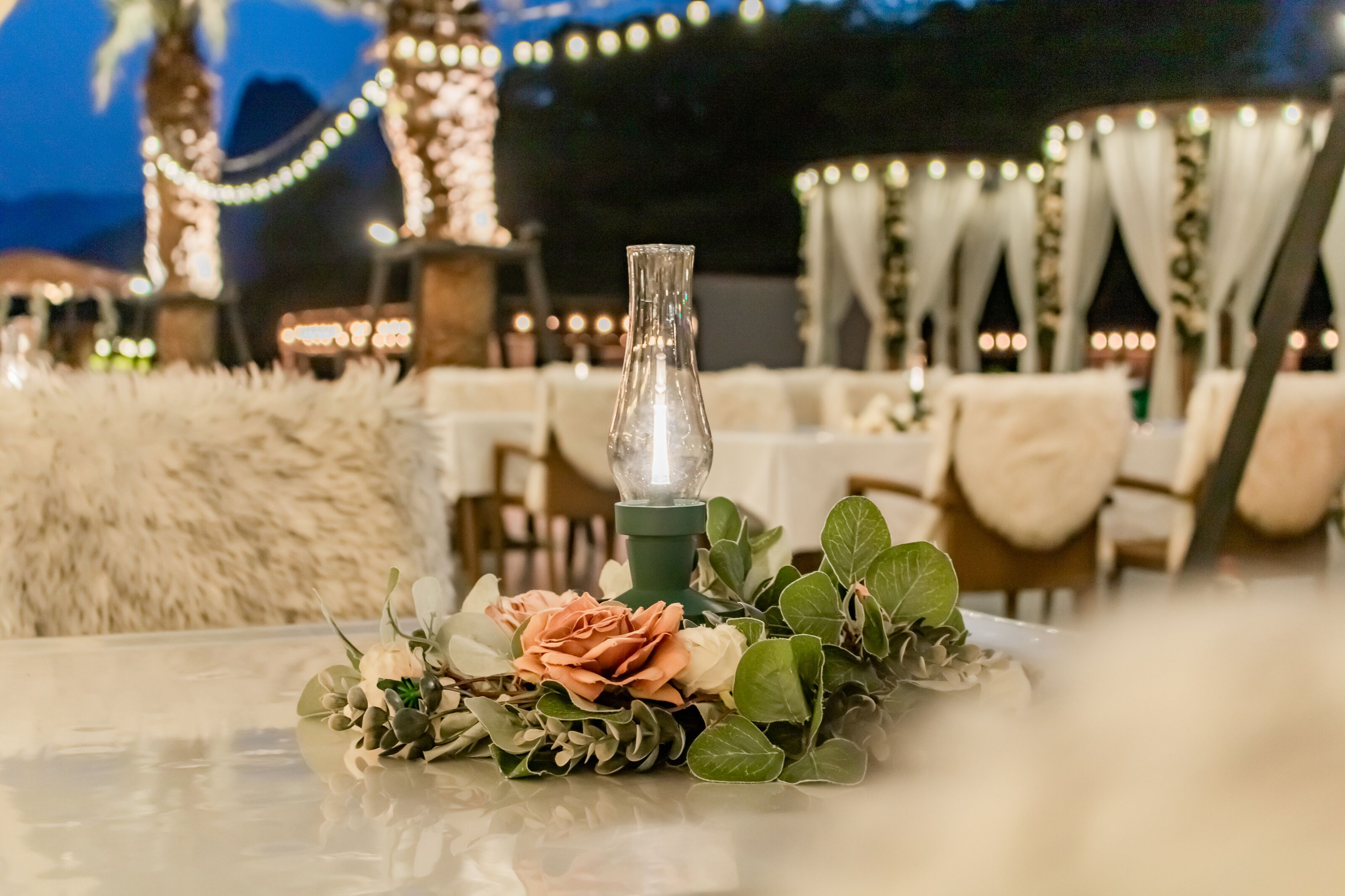 A table with a glass bottle centerpiece, surrounded by greenery and a peach-colored flower.