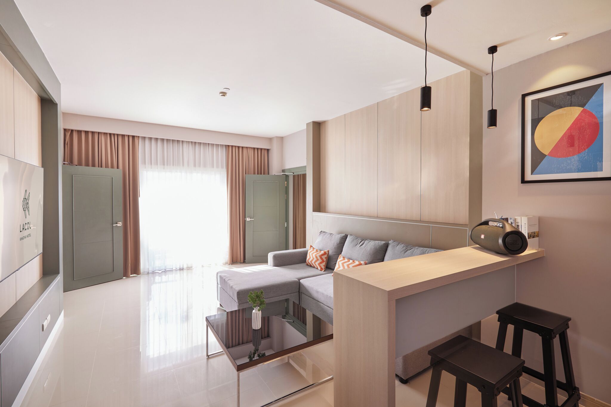 Una sala de estar moderna con un sofá, una mesa de centro, un televisor y una cocina con mostrador y taburetes.