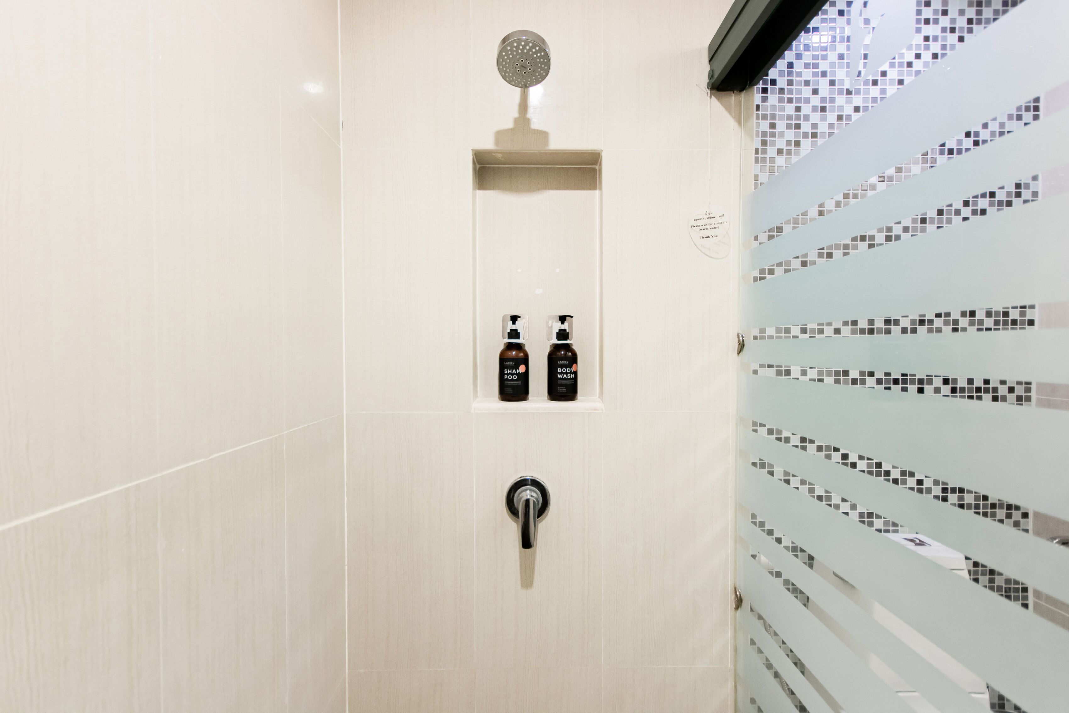 A modern bathroom with a shower, a toilet, and a sink. There are two bottles of shampoo and conditioner on the wall.