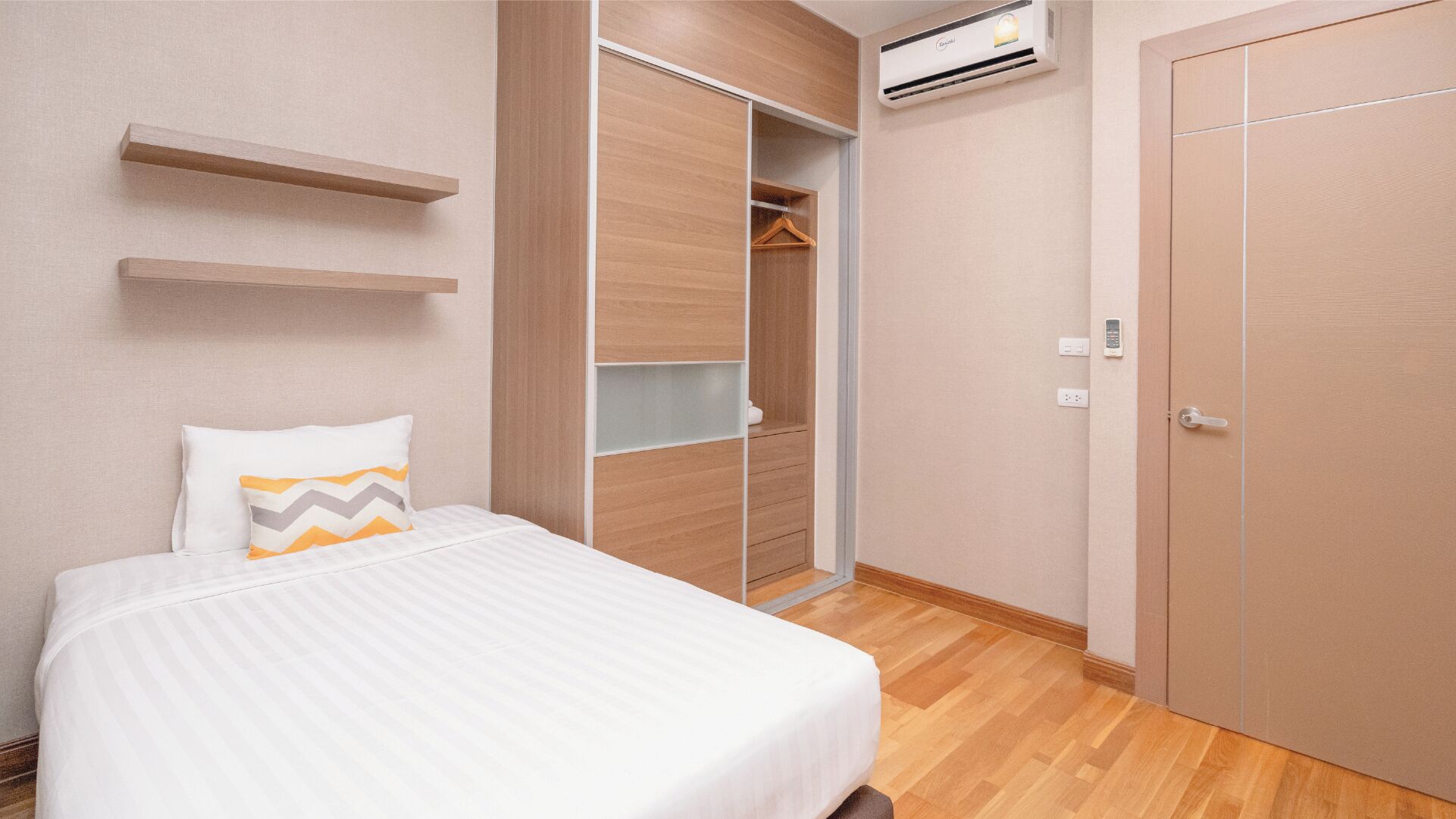 A bedroom with a bed, a wardrobe, a hanging closet, and an air conditioning unit.