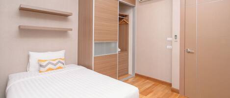 A bedroom with a bed, a wardrobe, a hanging closet, and an air conditioning unit.