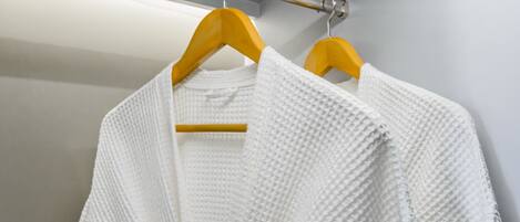A white textured garment hanging on a wooden hanger in a room with a metallic rod and a white wall.