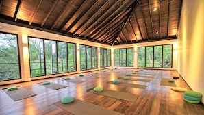A spacious room with wooden floors, large windows, and yoga mats arranged for practice.