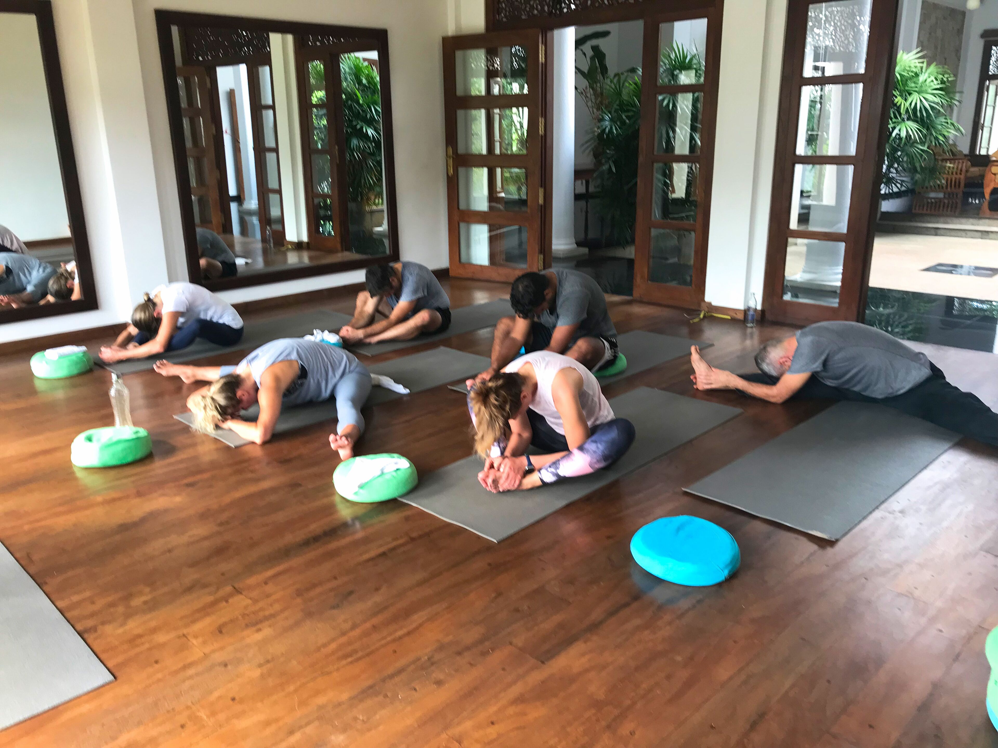 A yoga class in a room with wooden floors and large windows.