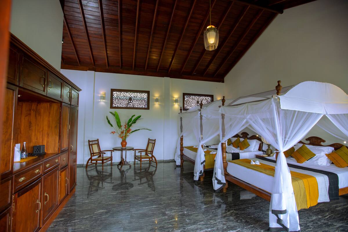 A room with a wooden ceiling, a bed with a canopy, a wooden cabinet, a table with chairs, and a potted plant.