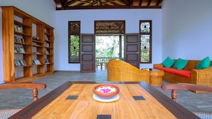 A wooden table with a bowl in the center, a wicker sofa with green cushions, and a wooden bookshelf.