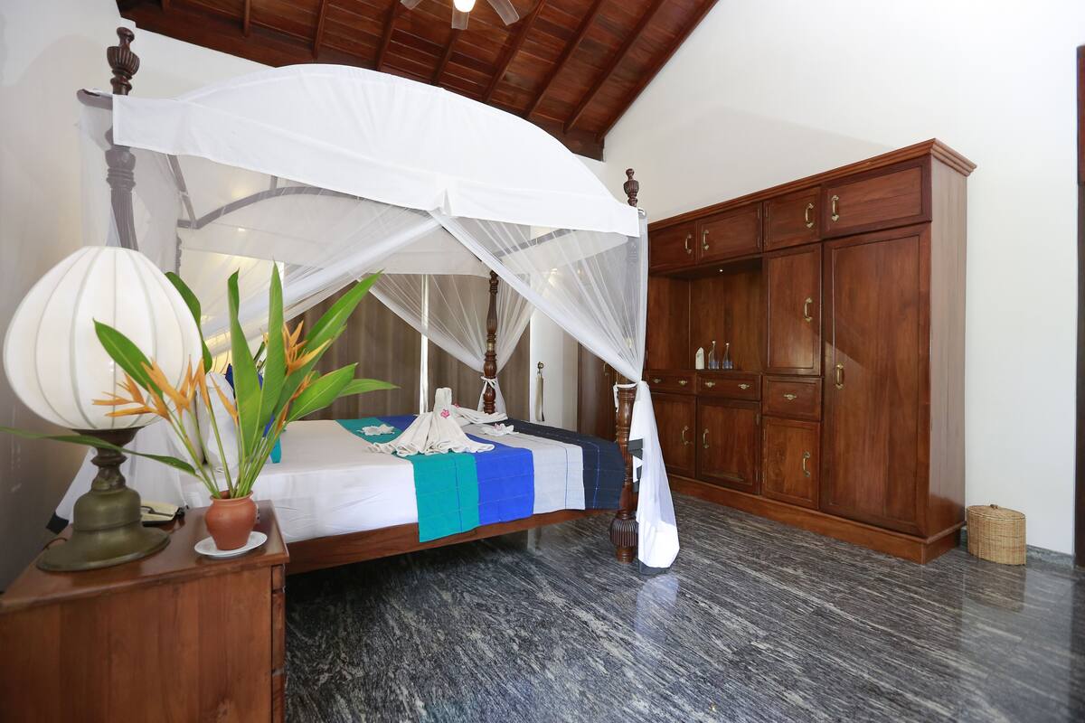 A bedroom with a four-poster bed, a wooden wardrobe, and a marble floor.