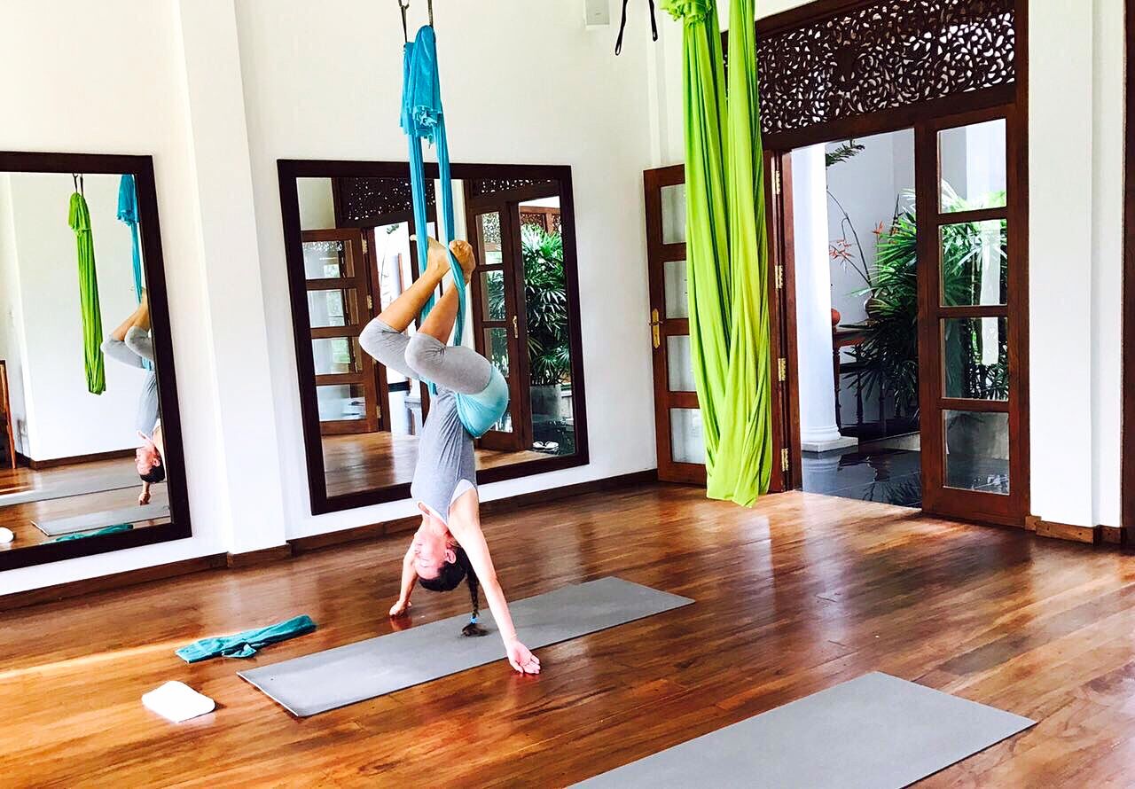 Un studio de yoga doté de planchers en bois, de tapis de yoga et de voiles aériennes vertes.