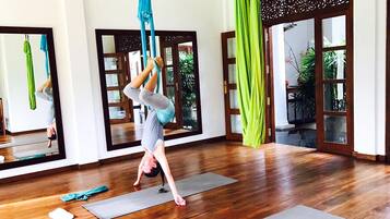 Un studio de yoga doté de planchers en bois, de tapis de yoga et de voiles aériennes vertes.