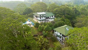 A large, two-story building with a green roof, surrounded by dense forest. There are several outdoor seating areas with blue umbrellas.