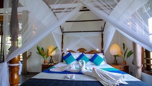 A four-poster bed with a canopy, two bedside tables with lamps, and a floral arrangement on each table.