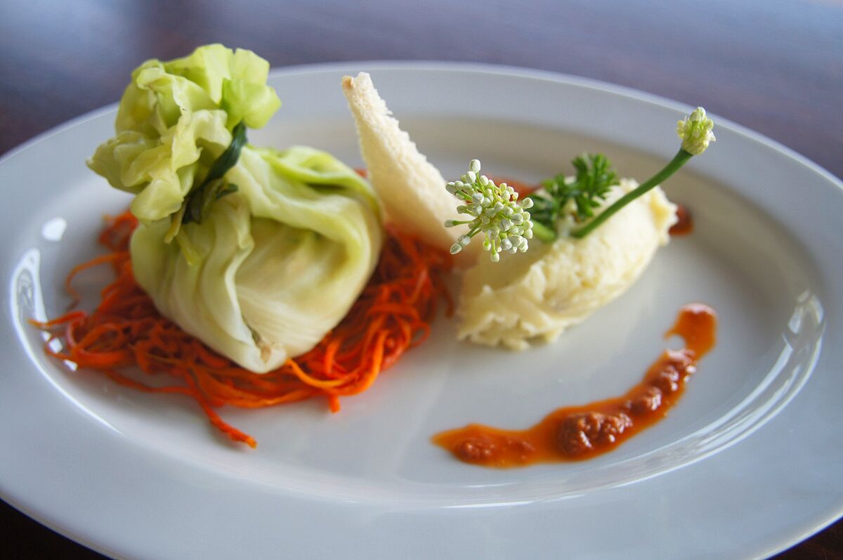 A white plate with a dish featuring shredded carrots, a cabbage roll, and a small dollop of sauce.