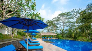 A poolside area with lounge chairs and umbrellas, surrounded by greenery and a clear sky. - Niyagama House (Galle)