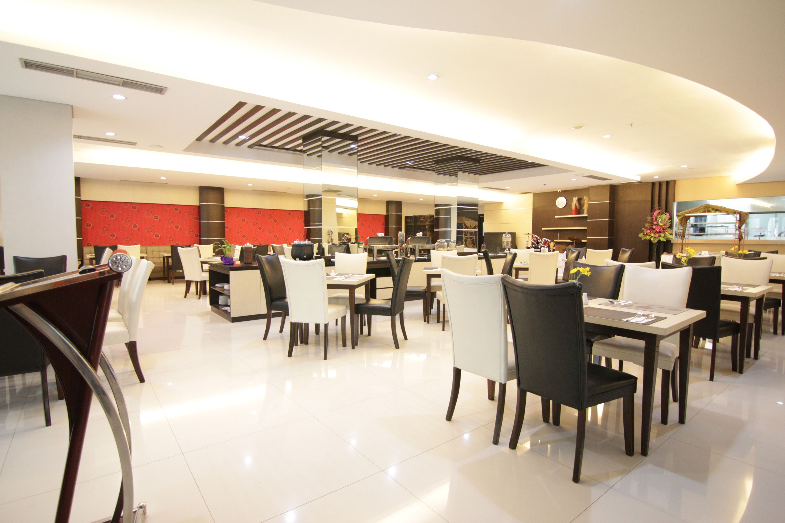 A spacious hotel dining area with multiple tables and chairs, a modern ceiling design, and a clean, well-lit environment.