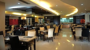 A modern restaurant with a bar area, multiple dining tables, and chairs. - Megaland Hotel (Surakarta)