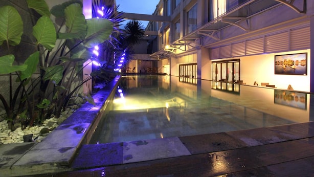 A modern hotel atrium with a glass-bottomed pool, surrounded by tropical plants and illuminated by blue lights. - Megaland Hotel (Surakarta)