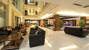 A spacious lobby with multiple seating areas, a reception desk, and a high ceiling with natural light. - Megaland Hotel (Surakarta)