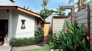 A modern house with a wooden deck, a pathway leading to the entrance, and lush tropical plants. - Belukar Villas (Gili Trawangan)