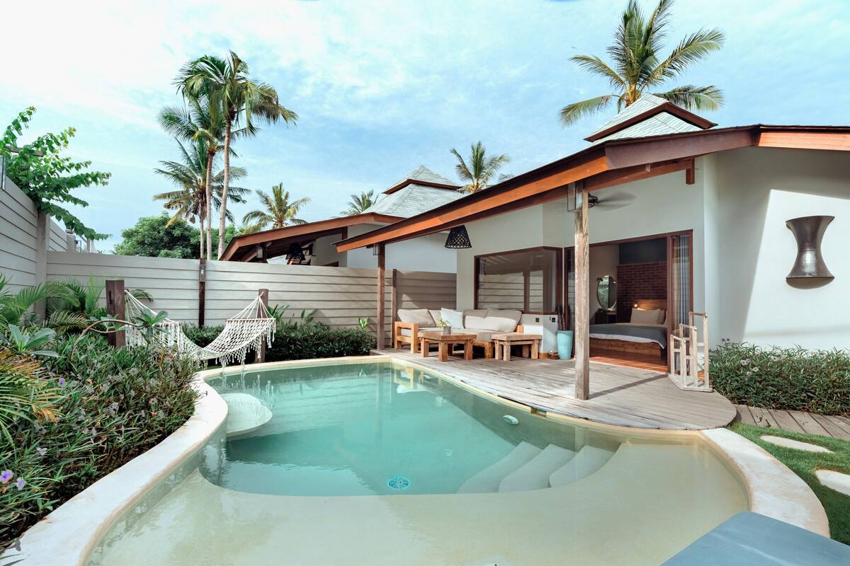 Un espace aménagé au bord de la piscine, avec une terrasse en bois, des sièges d’extérieur et un hamac.