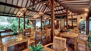 An indoor dining area with wooden tables and chairs, a high ceiling with exposed beams, and a menu board. - Belukar Villas (Gili Trawangan)