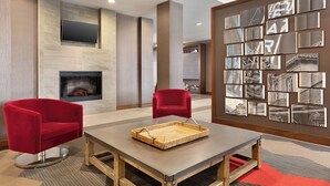 A modern lobby with a fireplace, two red chairs, a table with a tray, and a wall with framed pictures. - Four Points by Sheraton Fargo Medical Center (Fargo)