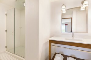 Une salle de bain moderne avec une douche à l’italienne en verre, un lavabo blanc avec un meuble-vasque en bois et un grand miroir au-dessus du meuble-vasque.
