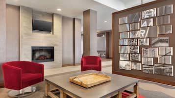 A modern lobby with a fireplace, red chairs, a table with a woven tray, and a wall with framed artwork.