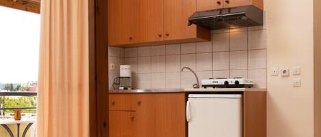 A compact hotel room with a kitchenette, a bed, and a view of the outdoors.
