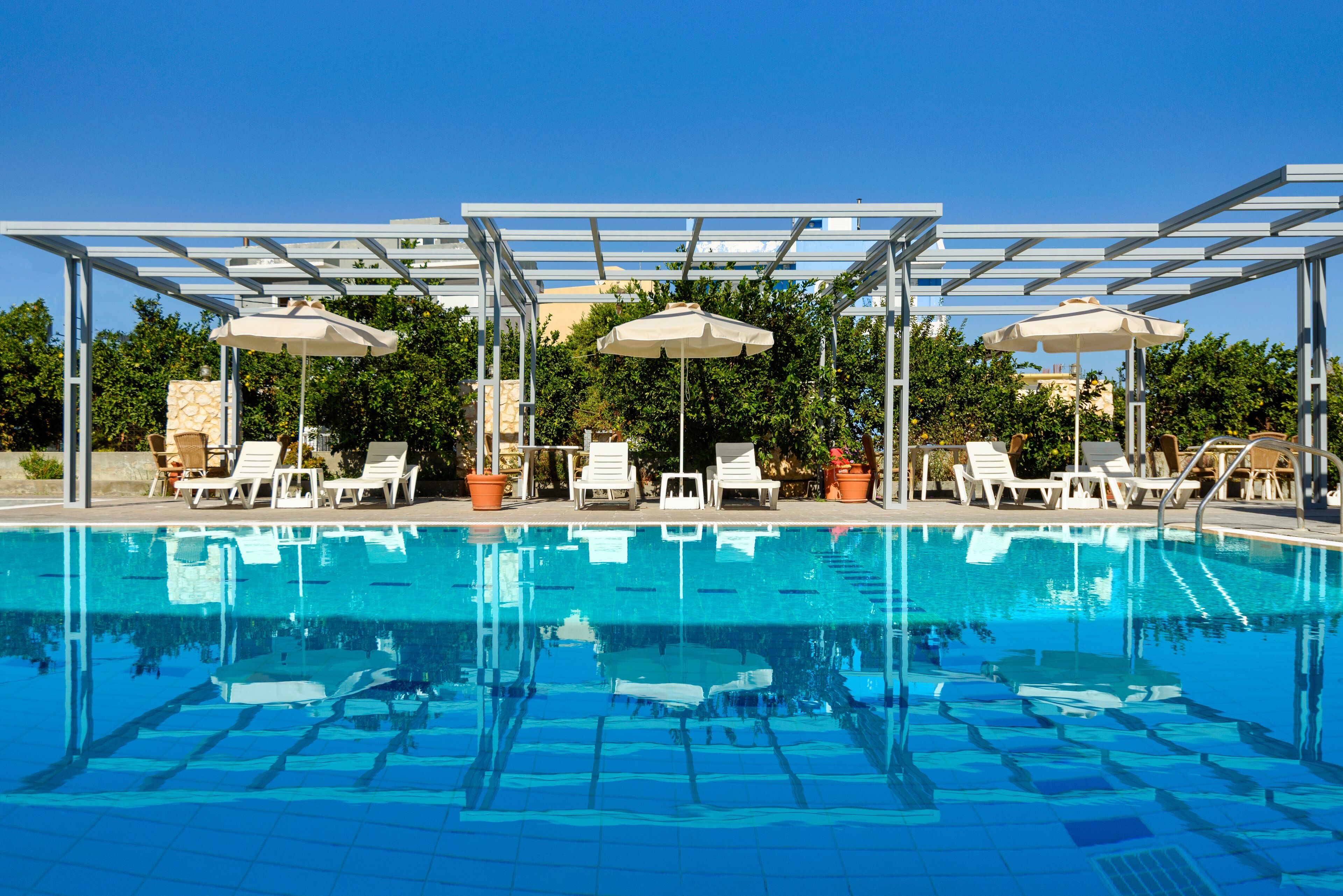 Una piscina cristallina con lettini e ombrelloni sotto una pergola.