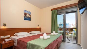Habitación de hotel con cama, mesita de noche, teléfono, un cuadro en la pared y balcón con vistas a edificios.