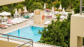 Zona de piscina con sillones de descanso y sombrillas, rodeada de vegetación.