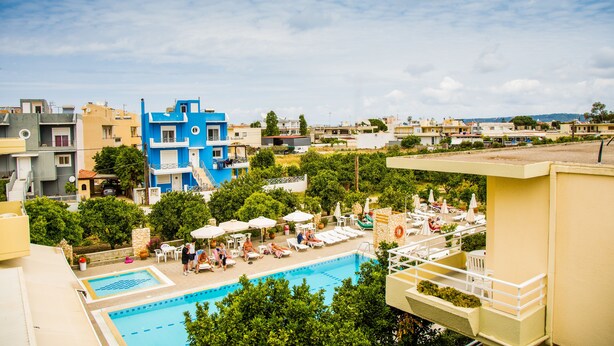 Un área de piscina en la azotea con sillones de descanso y sombrillas, rodeada de edificios con balcones.