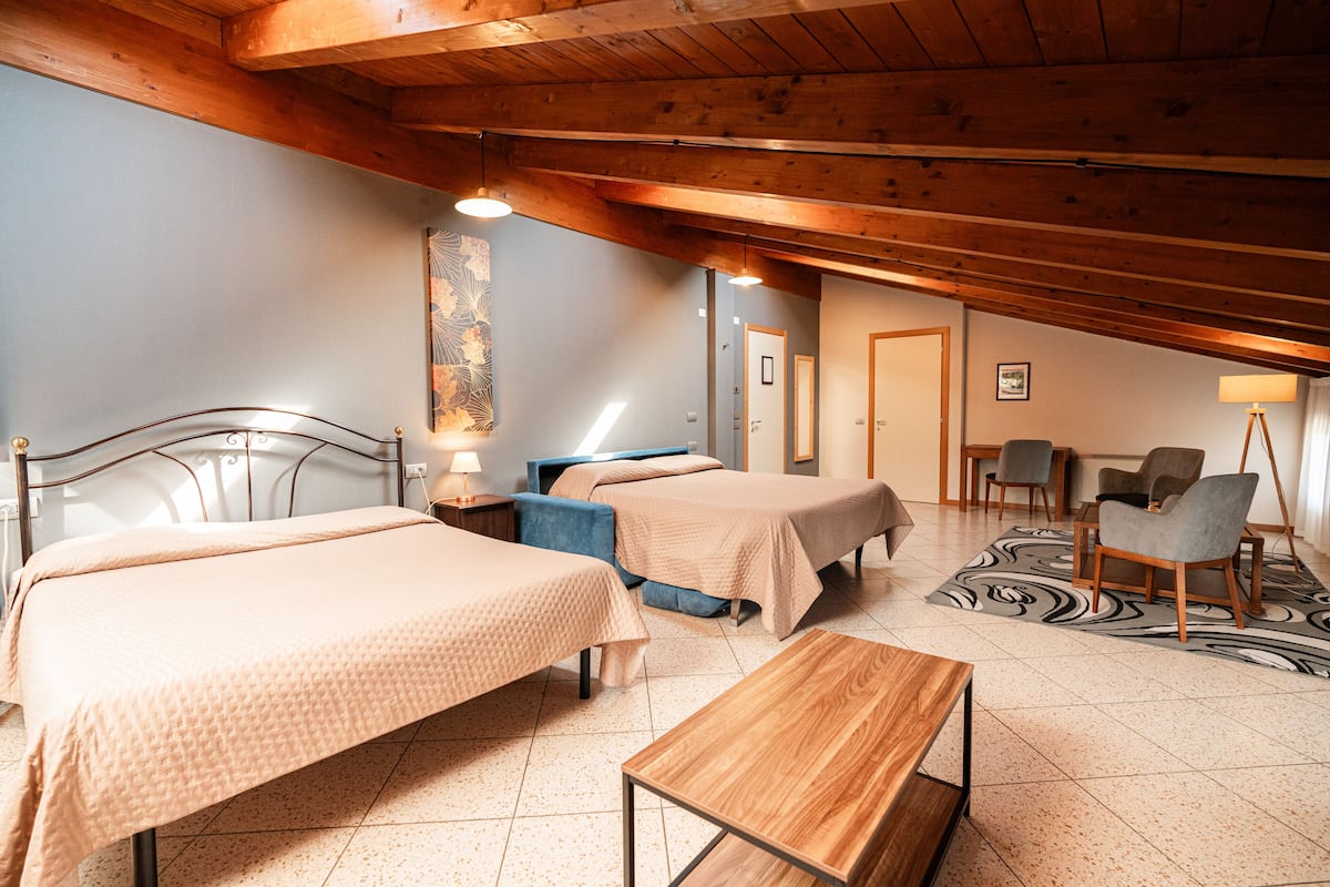 A hotel room with two beds, a wooden table, a blue chair, and a patterned rug.