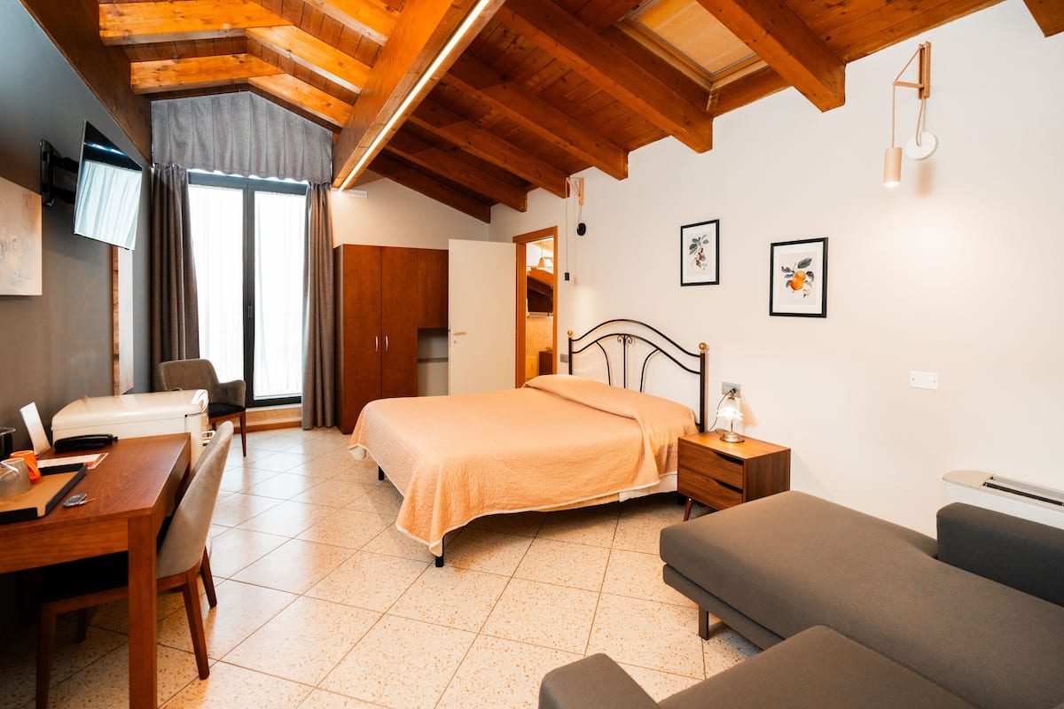 A bedroom with a bed, bedside table, lamp, and a desk with a chair.